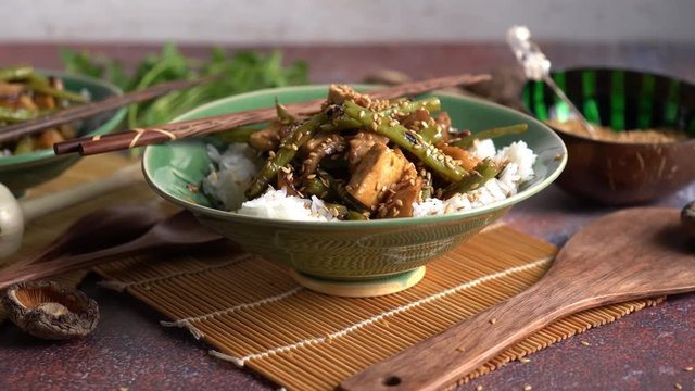 Trucking pull back holding focus on bowl of Szechuan greens beans and tofu with sesame seeds.