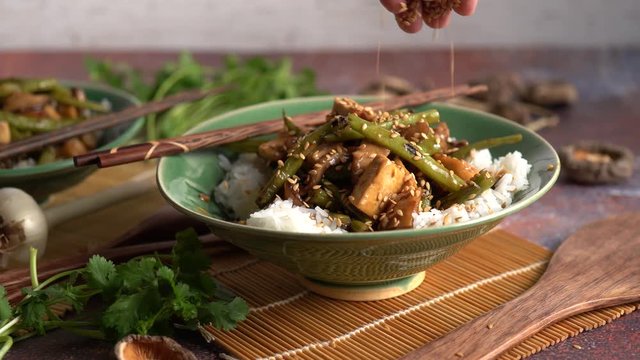 Closeup of Szechuan green beans and tofu with sesame seeds dropping onto it.