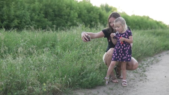 Beautiful young mother makes selfie with her daughter on the phone. A woman is photographed with her daughter in the field and watch pictures laughing