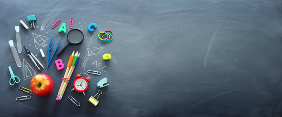 education and back to school concept. shapes cut from paper and painted of backpack, books, chemistry flask and apple over classroom blackboard with funny sketches. top view, flat lay