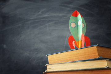 education and back to school concept. cardboard rocket over books in front of classroom blackboard