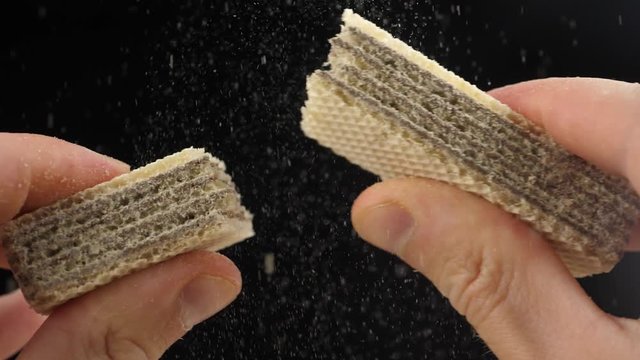 Chocolate waffle breaks down on a close-up. Men's fingers hold a wafer with a chocolate filling, and then break it in half. Slow motion.