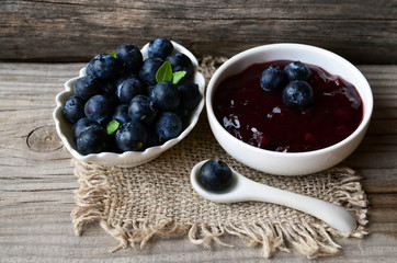 Fresh blueberry jam in a white bowl and freshly picked blueberries on old wooden background.Homemade food concept.