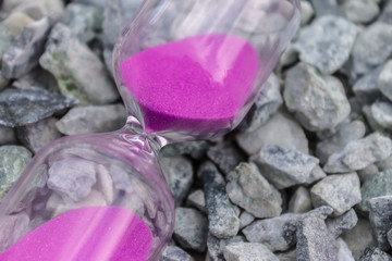 Hourglass with pink sand on small stones, symbol of time