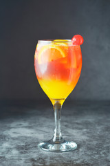 Summer cocktail. Orange juice with mint, syrop, fruit slices and cherry with ice. Dark background.