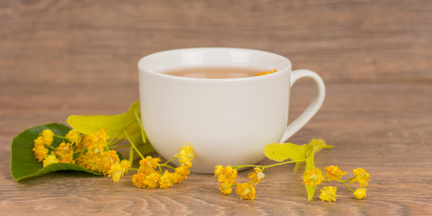 linden summer tea in white cup on wooden table, healthy and tasty hot drink