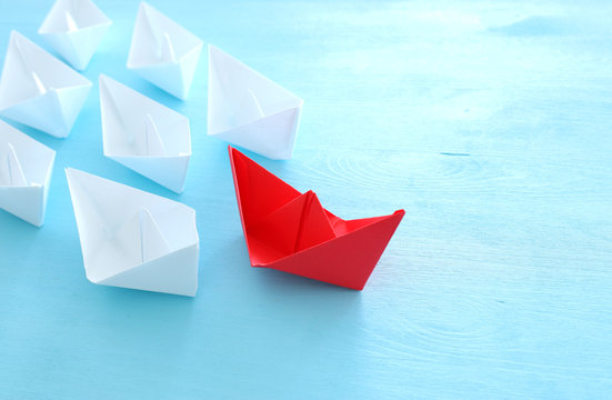 business. Leadership concept image with paper boats on blue wooden background. One leader guiding others.