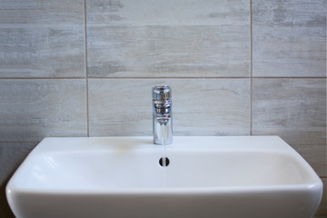 White ceramic sink and nickel-plated brass metallic single-lever tap, faucet  with running water in the bathroom.