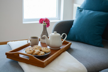 Fototapeta na wymiar Cozy mornings. Breakfast in the living room. Coffee or tea with cookies on a wooden tray with pink flowers in vase. 