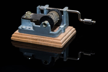 Small hurdy gurdy music box on black shiny reflecting surface close up shot.