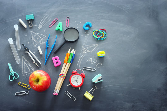 education and back to school concept. shapes cut from paper and painted of backpack, books, chemistry flask and apple over classroom blackboard with funny sketches. top view, flat lay