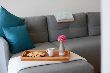 Cozy mornings. Breakfast in the living room. Coffee or tea with cookies on a wooden tray with pink flowers in vase. 