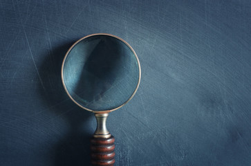 vintage magnifying mlass with wooden handle over chalkboard background. top view, flat lay