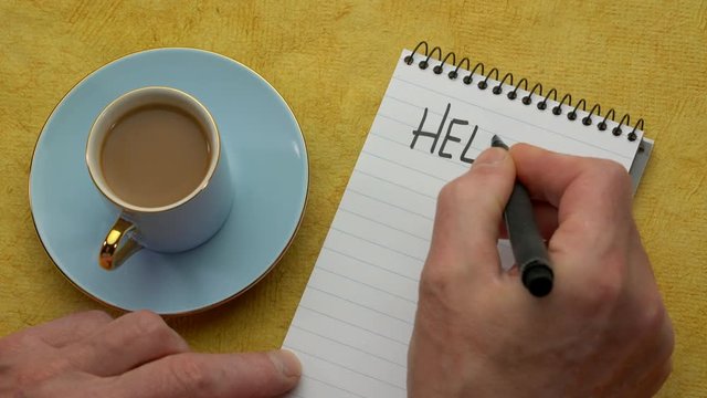 Hello August - a man hand writing a note with a black marker in a notebook, overhead view with a cup of coffee