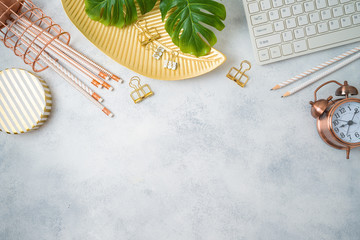 Flat lay home office feminine table with golden accessories, computer keyboard and tropical leaves...