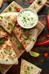 Mexican quesadilla with chicken, corn, black beans, cheese, vegetables, lime and yogurt sauce on wooden board