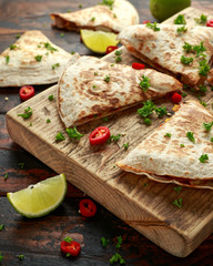 Mexican quesadilla with chicken, corn, black beans, cheese, vegetables, lime and yogurt sauce on wooden board