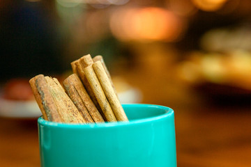 Cinnamon sticks in a glass on the table. Multicolored festive bokeh on background.