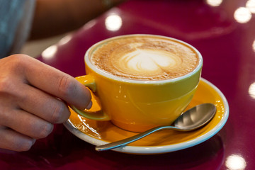 A large cup of cappuccino with a heart on the skin in the hand of a girl sitting in a restaurant. Close-up.