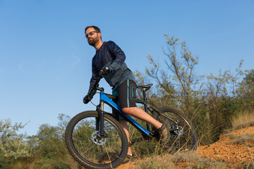 Fototapeta premium Cyclist in shorts and jersey on a modern carbon hardtail bike with an air suspension fork rides off-road on the orange-red hills at sunset evening in summer 