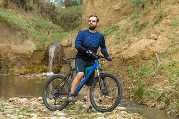 Obraz premium Cyclist in shorts and jersey on a modern carbon hardtail bike with an air suspension fork rides off-road on the orange-red hills at sunset evening in summer 