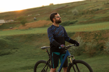 Obraz premium Cyclist in shorts and jersey on a modern carbon hardtail bike with an air suspension fork rides off-road on the orange-red hills at sunset evening in summer 