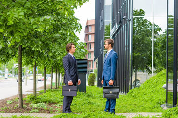Confident business men talking in front of modern office building. Businessman and his colleague. Banking and financial market.
