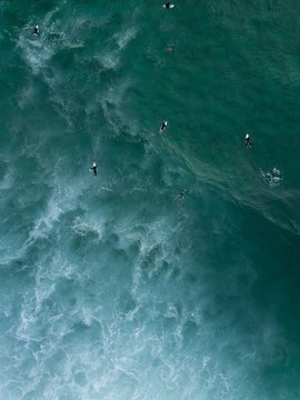 Aerial shot of surfers swimming laying on their boards in the sea waiting for strong waves to come
