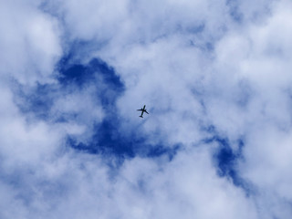 Airplane silhouette on a background of blue sky and white clouds. Passenger plane is flying high in the sky.