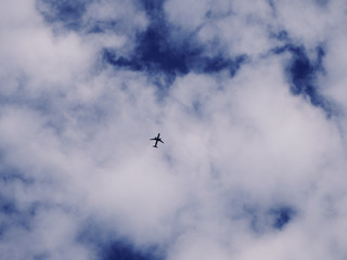 Airplane silhouette on a background of blue sky and white clouds. Passenger plane is flying high in the sky.