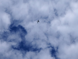 Airplane silhouette on a background of blue sky and white clouds. Passenger plane is flying high in the sky.