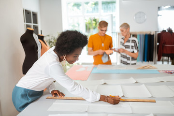 Smiling pretty female tailor drawing a paper pattern