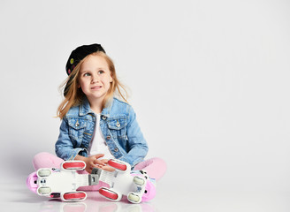 girl sits on the rollers in a blue denim and cap and smiles. Summer sports for children.