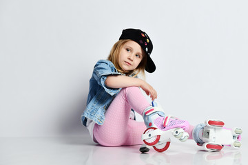 girl sits on the rollers in a blue denim and cap and smiles. Summer sports for children.