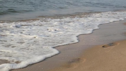Wave of the sea surf washes away footprints on a sandy beach