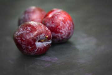 Three red plums on a black textured background.