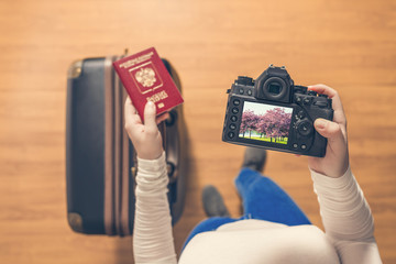 Top view on a girl looking a photos Flowering Sakura on her camera standing with suitcase in the airport. The girl returns home after trip to Japan.