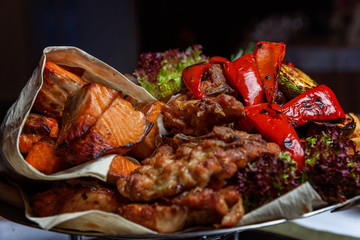 Mixed grill meat, fried vegetables and grilled salmon fish fillets decoration in warm dish. Assorted delicious grilled kebab served with herbs on platter. Restaurant menu plate
