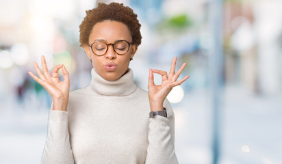 Young beautiful african american woman wearing glasses over isolated background relax and smiling with eyes closed doing meditation gesture with fingers. Yoga concept.