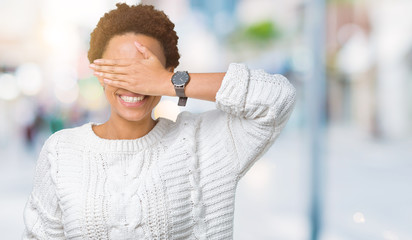 Beautiful young african american woman wearing sweater over isolated background smiling and laughing with hand on face covering eyes for surprise. Blind concept.