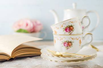 Cup of tea with book, teapot and rose flowers on blue background with vintage tone - Afternoon tea party concept