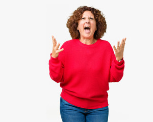 Beautiful middle ager senior woman red winter sweater over isolated background crazy and mad shouting and yelling with aggressive expression and arms raised. Frustration concept.