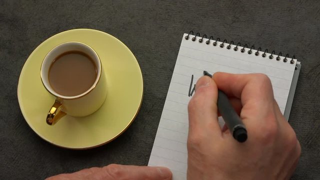 Way to go - a man hand writing a note with a black marker in a notebook, overhead view with a cup of coffee