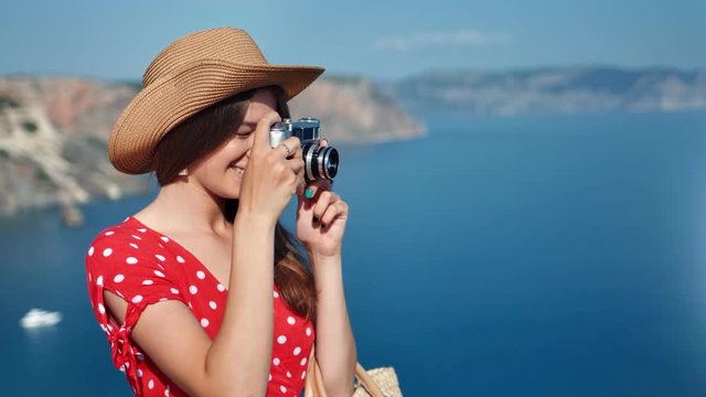 Happy travel glamour female in hat taking photo of nature seascape using camera medium close-up