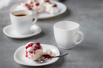 Homemade dessert Pavlova with raspberries on a white plate and two white cups of coffee on a gray table.