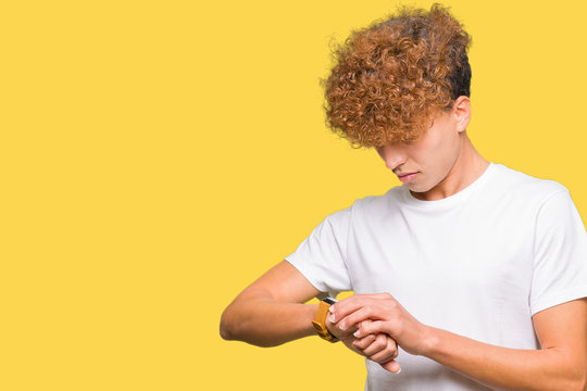 Young handsome man with afro hair wearing casual white t-shirt Checking the time on wrist watch, relaxed and confident