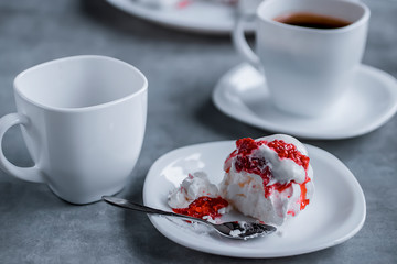 Homemade dessert Pavlova with raspberries on a white plate and two white cups of coffee on a gray table.
