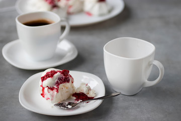 Homemade dessert Pavlova with raspberries on a white plate and two white cups of coffee on a gray table.