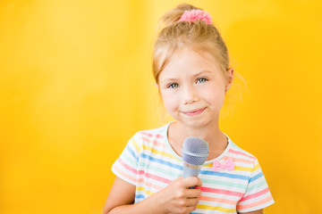 Happy little girl singing into a microphone the song on yellow background