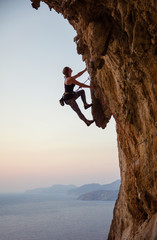 Young woman climbing challenging route at sunset - obrazy, fototapety, plakaty